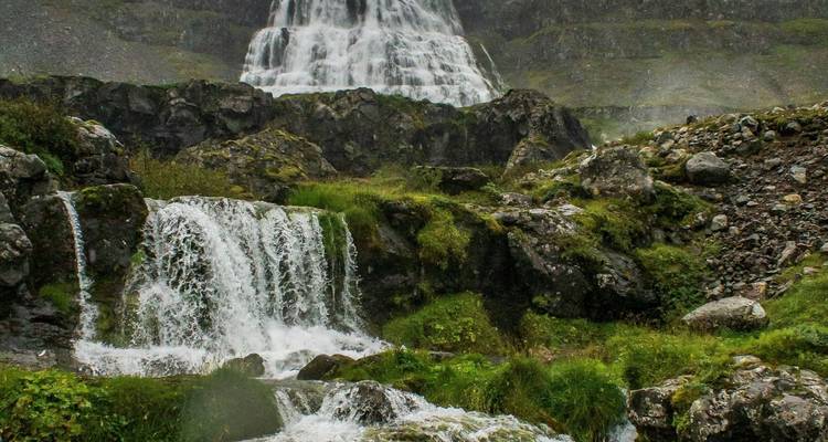 Rochers couverts de mousse et petites cascades sous un étage impressionnant d'une large chute d'eau dans une vallée accidentée.