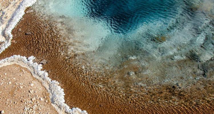 Close-up luchtfoto van een levendig blauw geothermisch bad omgeven door witte mineraalafsettingen en roestkleurige aarde.