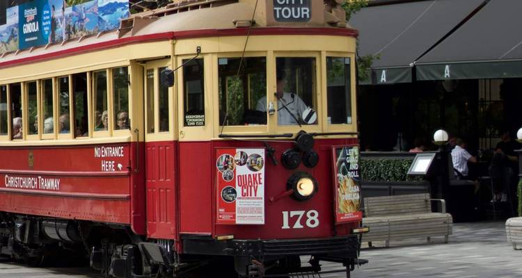 Historische rode en crème Christchurch erfgoedtram wacht op de stadstraat met rondleidingsposters.