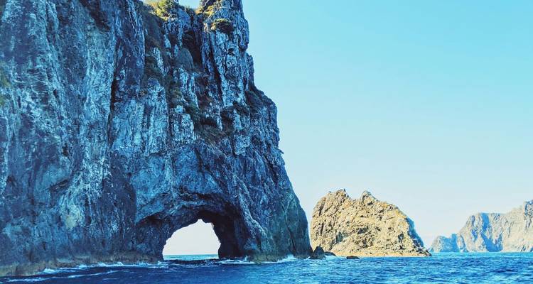 Towering coastal rock arch rising from vivid blue sea with clear sky.