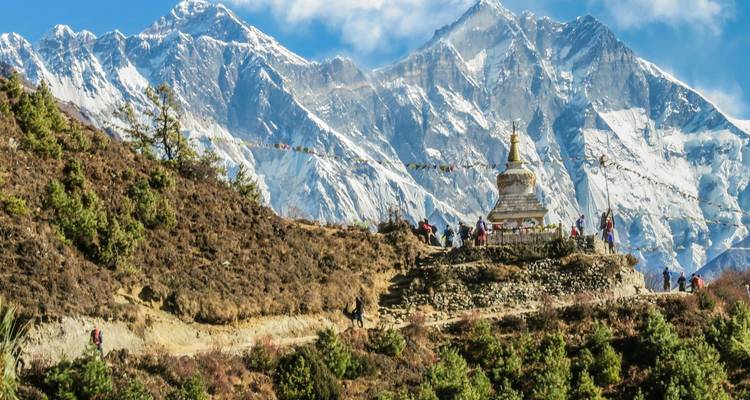 Crête bordée de drapeaux de prière avec stupa blanc surplombant le massif imposant de l'Everest sous un ciel dégagé.