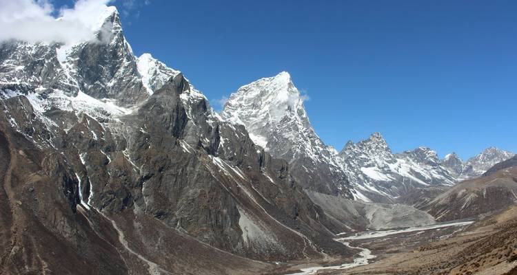 Vallée himalayenne austère et sauvage avec des pics rocheux à pic et un lit de rivière asséché sous un ciel bleu profond.
