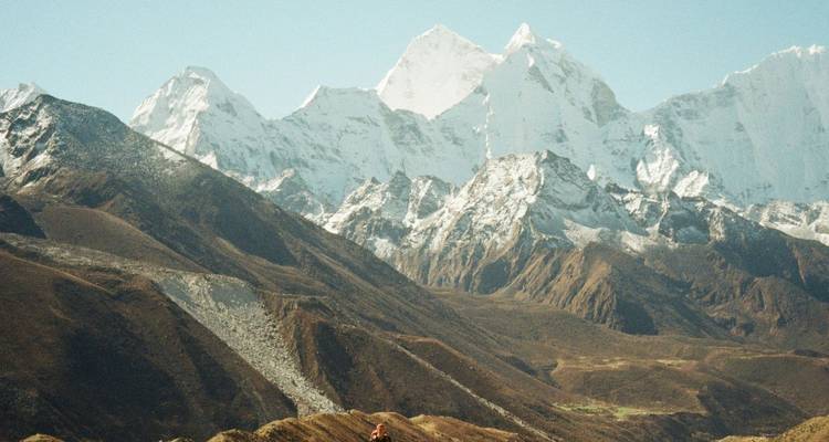 Photographie granuleuse prise de loin de sommets himalayens blancs s'élevant au-dessus de contreforts arides et bruns.