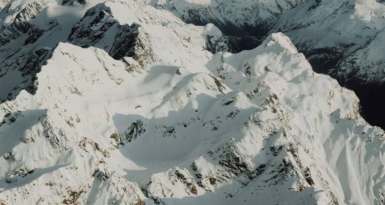 Vue aérienne de pics alpins escarpés couverts de neige et de crêtes abruptes sous une lumière douce.