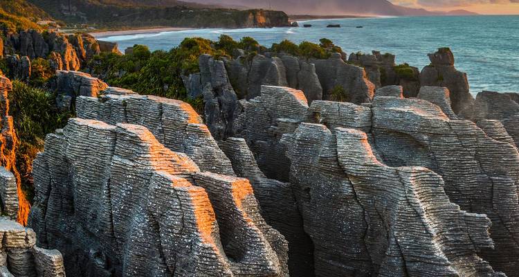 Las capas de piedra caliza de una costa escarpada brillan en naranja bajo la luz baja del sol junto a un mar azul.