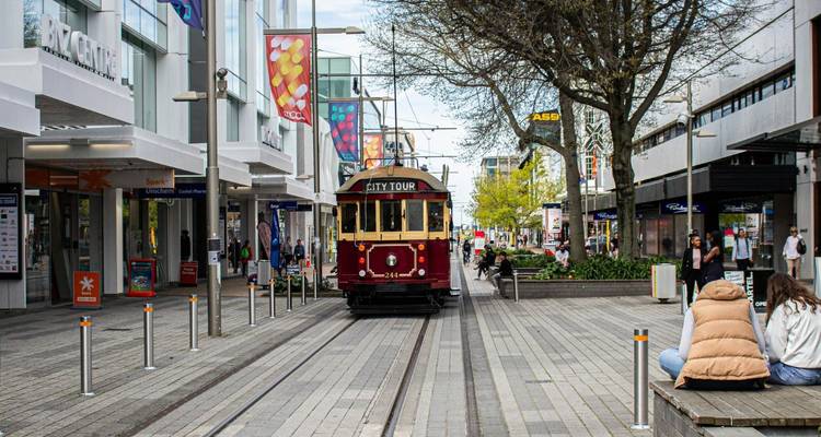 Straßenbahn fährt eine Fußgängerstraße mit Einkäufern und Sitzmöglichkeiten hinunter.