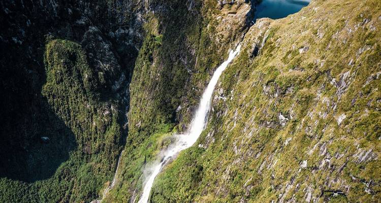 Aerial view of high waterfall plunging down steep forested cliffs into a remote valley