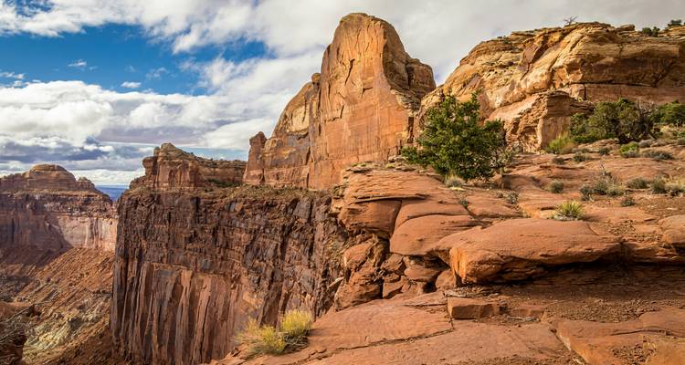 Los acantilados de roca roja y áspera caen dramáticamente en un cañón profundo bajo nubes dispersas