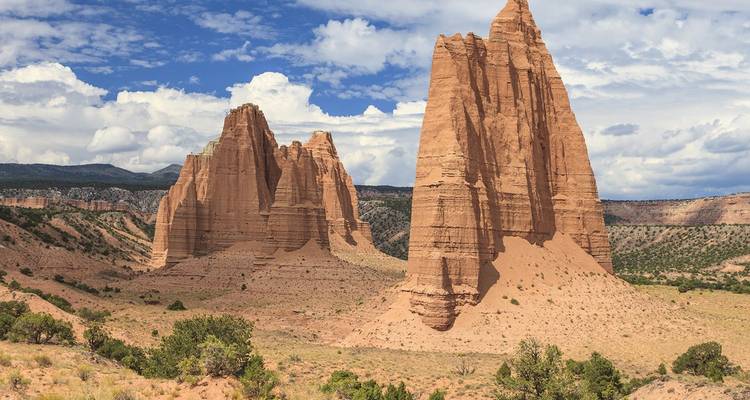 Formaciones de arenisca monolíticas y altas se elevan desde el piso del desierto alto bajo un cielo parcialmente nublado en Capitol Reef