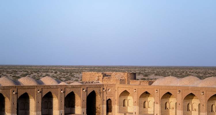 Wide-angle shot of a historic brick caravanserai set against an endless flat steppe under a pale blue sky.