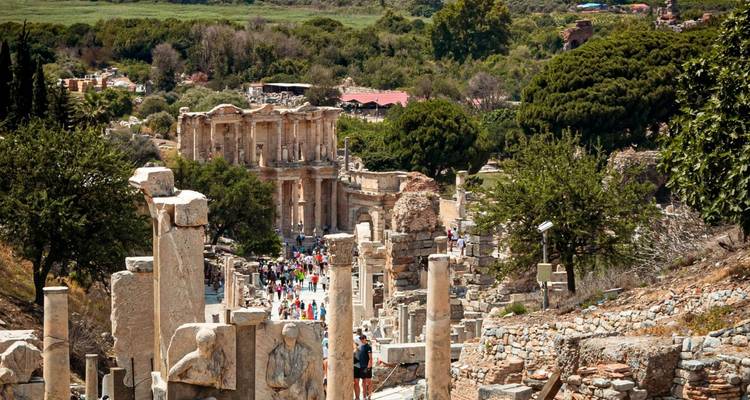Perspective along a ruined marble avenue leading to the grand façade of the Library of Celsus at Ephesus with crowds of visitors.