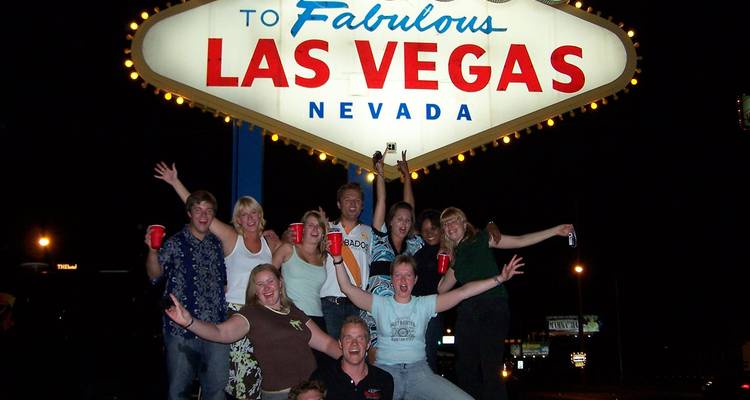 Grupo alegre celebrando frente al icónico letrero de bienvenida de Las Vegas iluminado por la noche.