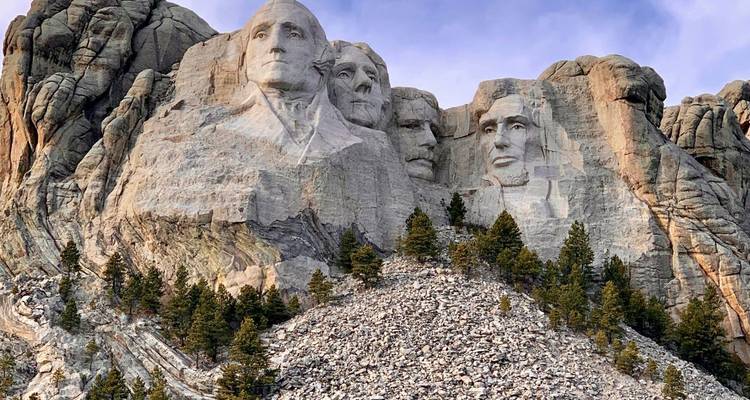Granite cliff with the carved faces of four US presidents at Mount Rushmore surrounded by scattered pines.