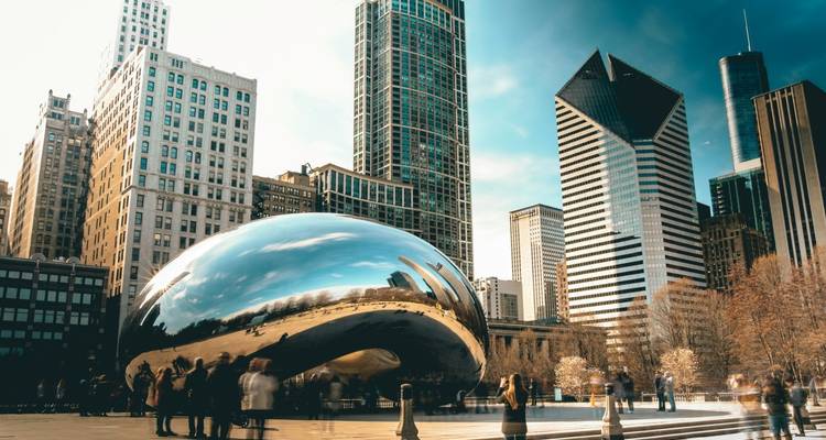 Chicago’s shiny Cloud Gate sculpture reflects the surrounding skyscrapers and blurred crowds on a sunny day.