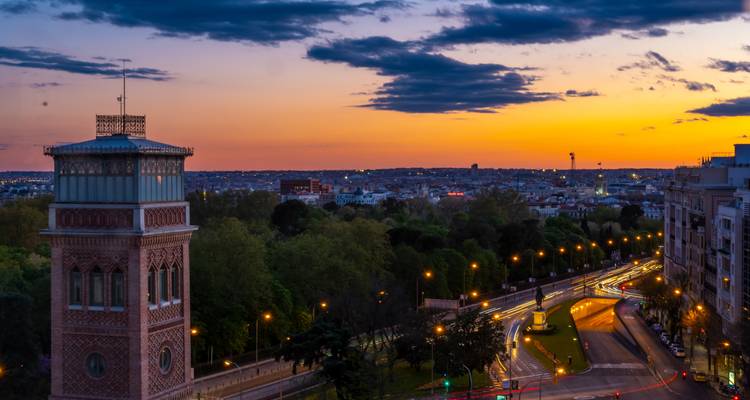 Colorful sunset over Madrid skyline with winding car light trails beside a historic brick tower