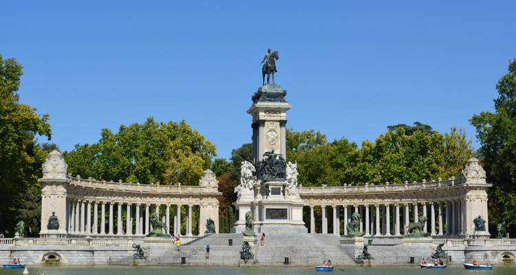Monument to Alfonso XII framed by sweeping colonnade beside a boating lake in Madrid’s Retiro Park