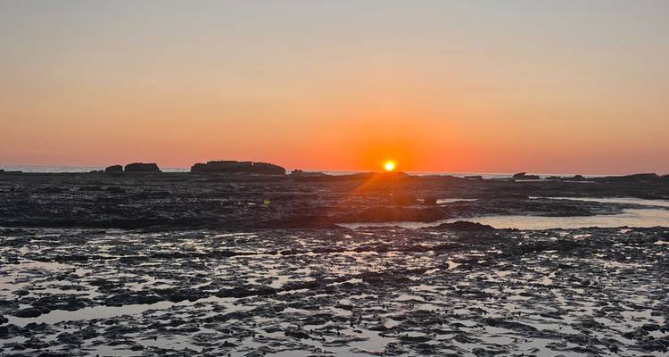 Un brillante sol naranja se pone sobre las marismas rocosas reflejando tonos cálidos