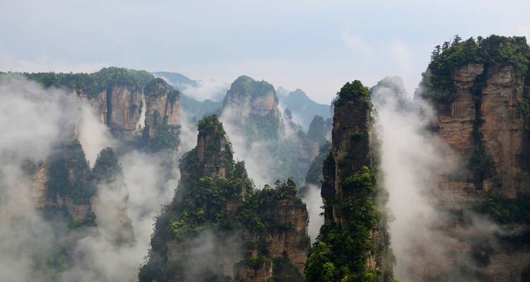 Misty sandstone spires emerging from clouds in Zhangjiajie creating a dramatic scene.