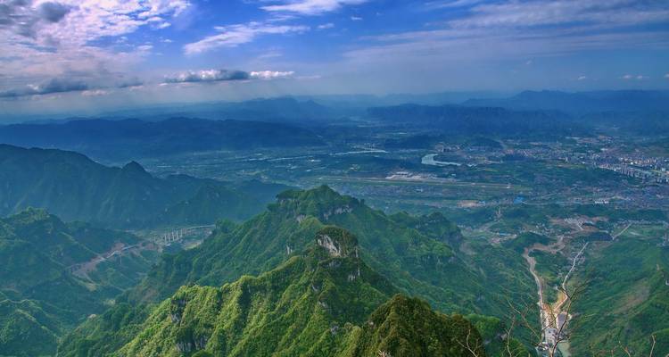 Expansive aerial panorama of misty green mountains and valley towns in Hunan province.