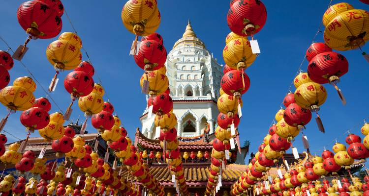 Filas de linternas rojas y amarillas cuelgan frente a una torre pagoda ornamentada contra un cielo azul despejado.
