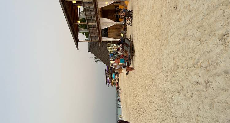 Bar de playa con tumbonas y clientes en arena blanca al atardecer
