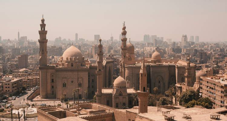 Vista aérea brumosa de las históricas mezquitas de El Cairo dominando el horizonte entre los edificios modernos de la ciudad.