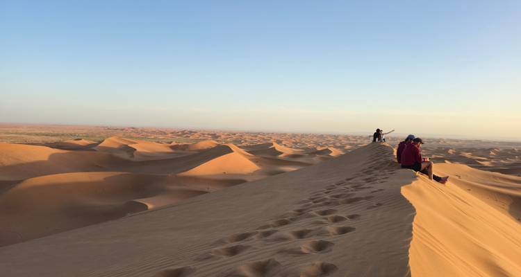 Long ridge of footprints atop a dune where travelers sit enjoying vast desert vistas.