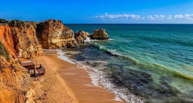 Des falaises stratifiées colorées, une plage de sable fin et des vagues d'eau turquoise le long du littoral de l'Algarve.