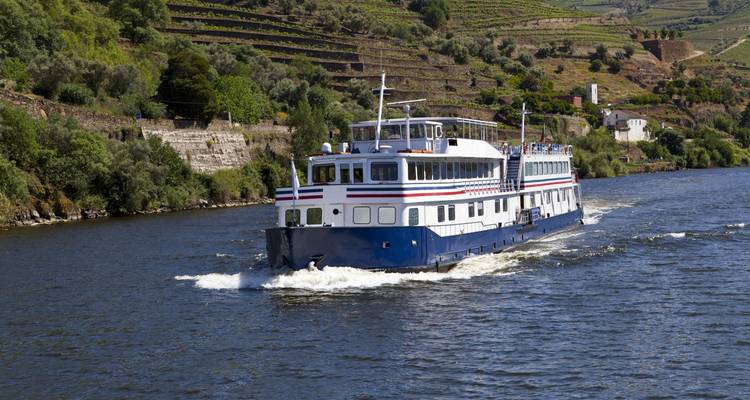 Bateau de croisière fluviale naviguant sur le fleuve Douro entouré de vignobles en terrasses.