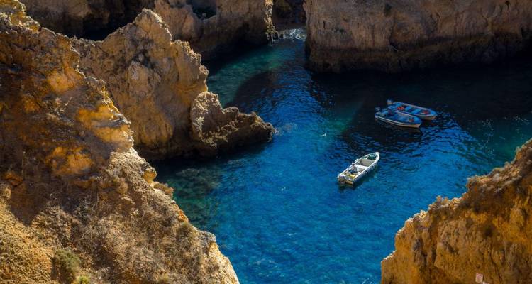 De petits bateaux flottant dans une crique d'émeraude encadrée par des falaises imposantes sculptées par la mer à Ponta da Piedade.