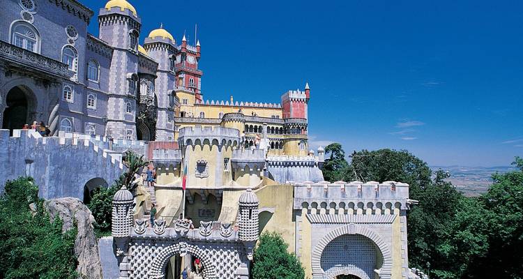 Vibrante Palacio de Pena con torres y cúpulas coloridas encaramadas sobre colinas boscosas bajo un cielo despejado.