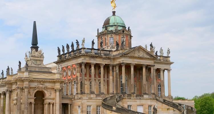 Palais Neues de style baroque à Potsdam avec des statues ornées et un escalier en spirale sous un ciel dégagé.