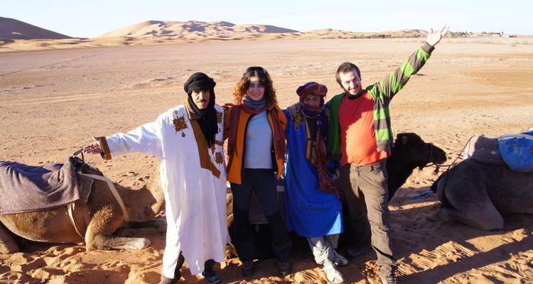 Travellers and Berber guides posing with resting camels on a vast Saharan dune plain.