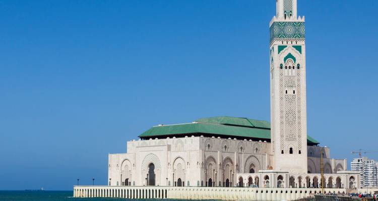 Perfil de la orilla del mar de la Mezquita Hassan II extendiéndose a lo largo de un muelle sobre aguas turquesas en un día despejado.