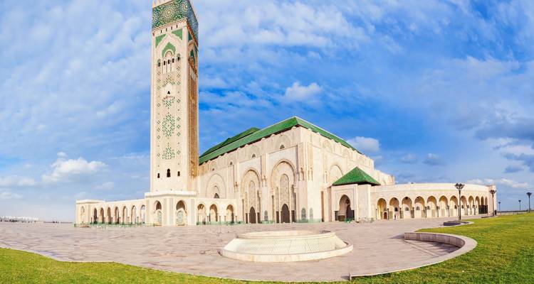 Vista de gran angular de la Mezquita Hassan II con una plaza expansiva bajo un cielo azul parcialmente nublado.
