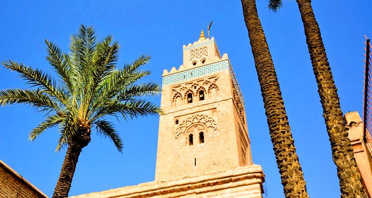 El minarete de la Mezquita Koutoubia elevándose junto a palmeras contra un vivido cielo azul de Marrakech.