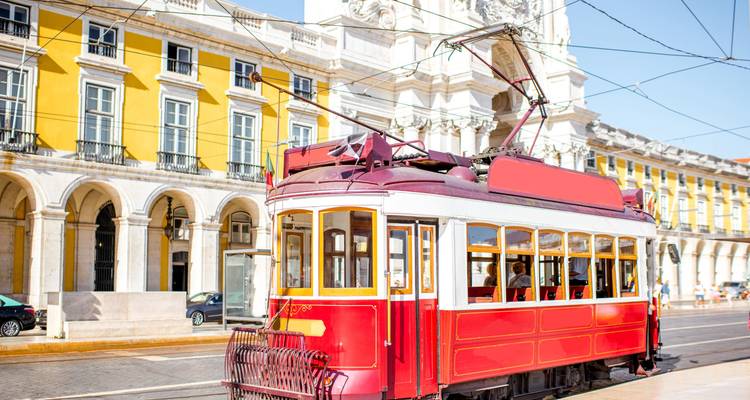 Rode historische tram op het Praça do Comércio in Lissabon met een felgeel gevelwerk erachter.