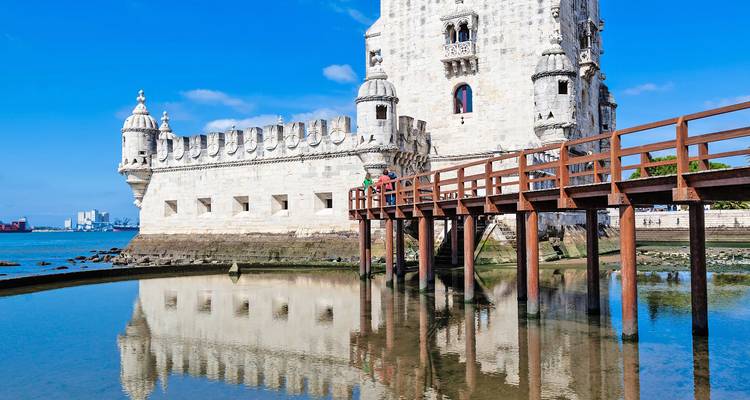 Belem Tower reflected in shallow water against a bright blue sky