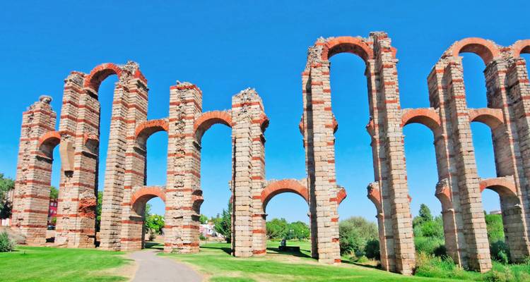 Tall arches of the ancient Aqueduct of Los Milagros stretching across green parkland