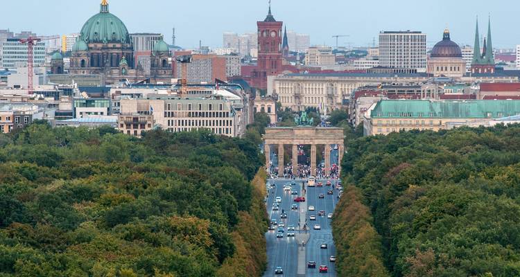 Paisaje urbano elevado con un bulevar atravesando un parque verde hacia la Puerta de Brandeburgo y los puntos de referencia de Berlín.