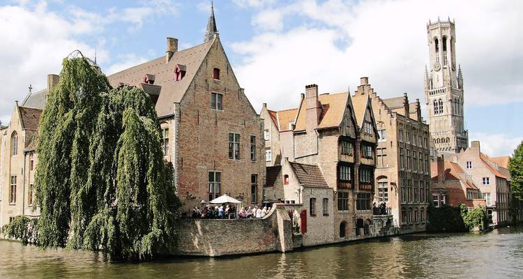 Les maisons historiques en brique et le Beffroi de Bruges bordent un canal tranquille reflétant l'architecture médiévale.