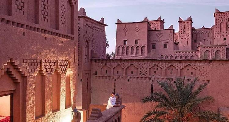 Couple wrapped in blankets on the ramparts of an earth-toned kasbah at dusk in Ait Benhaddou.