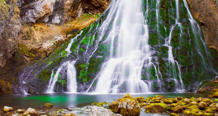 Una cascada sedosa cae sobre rocas cubiertas de musgo hacia una piscina esmeralda cristalina.
