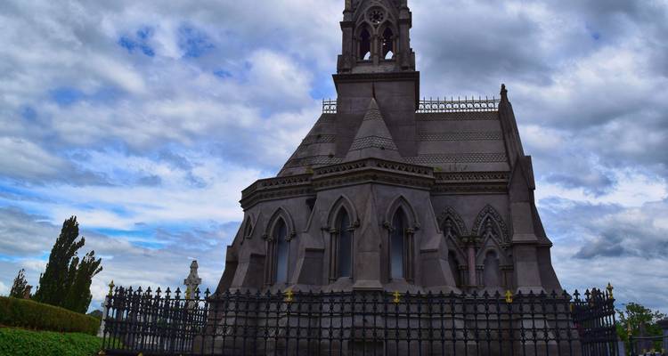 Gothic stone mausoleum with ornate spire under dramatic cloudy skies in Belfast.