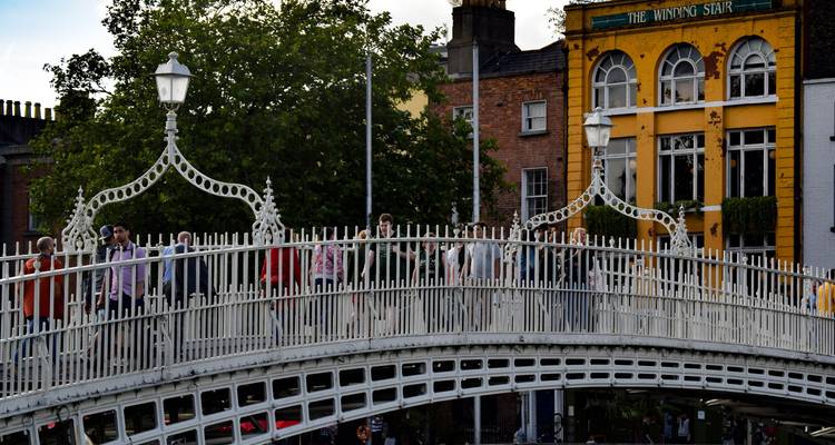 Crowds crossing the ornate white Ha’penny Bridge over the River Liffey in Dublin.
