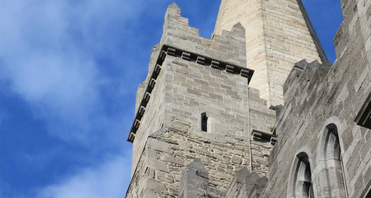 Stone tower and spire of a medieval church rising into a clear blue sky in Dublin.