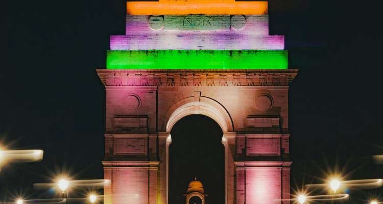 The India Gate monument in Delhi illuminated in tricolor lights against the night sky.