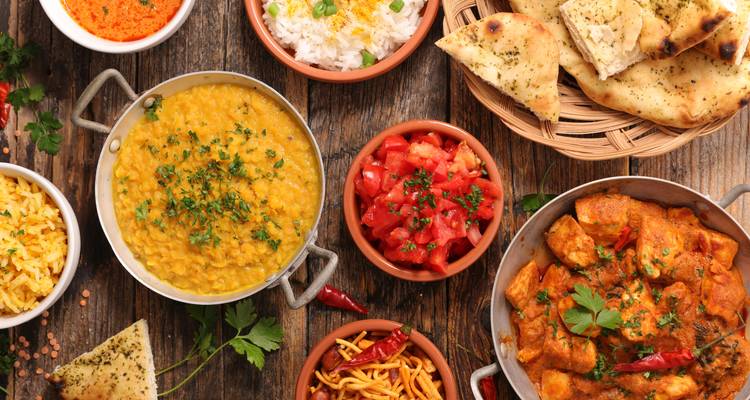 Colorful assortment of Indian dishes including dal, curry, naan and chutneys arranged on rustic wooden table.