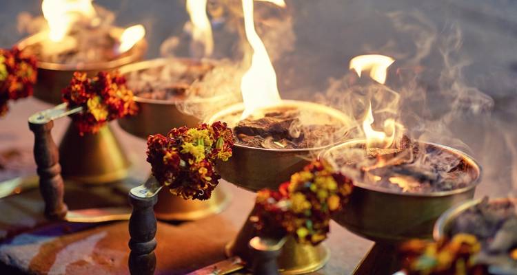 Close-up of ritual brass bowls with burning incense and vibrant marigold garlands during a Hindu ceremony.