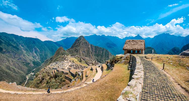 Panoramisch uitzicht op de citadel van Machu Picchu, slingerende paden en omringende groene bergen onder een helderblauwe hemel.